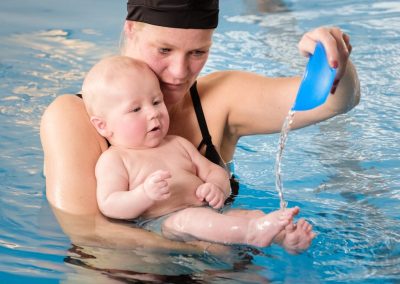 Mama beim Babyschwimmen gießt Wasser