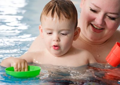 Mama beim Babyschwimmen spielt mit Baby